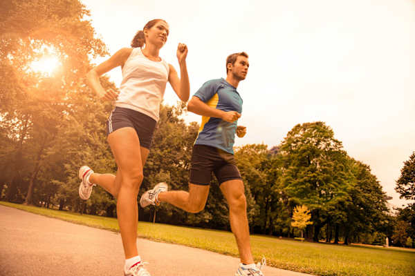 A man and a woman are running on a road in a park.